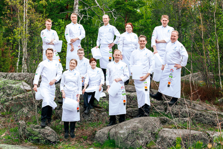 Suomen kokkimaajoukkue seisoo kalliolla kokinpuvut päällä